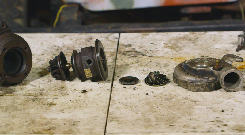 The turbocharger torn apart. The turbine housing and wheel are on the left, while the compressor housing is the cast aluminum one on the right, and the compressor wheel is sitting flat on the table. Photo: Jared Auslander